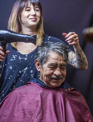 A lady is blow drying a young senior grey hair in a burgundy cape.