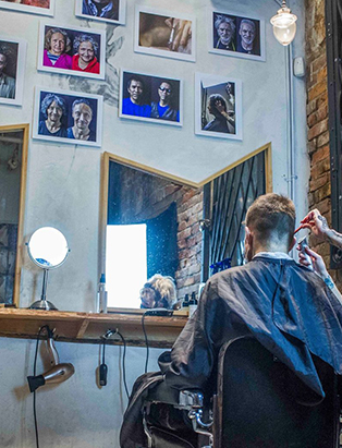 A guy sitting infront of a mirror receiving hair services. 