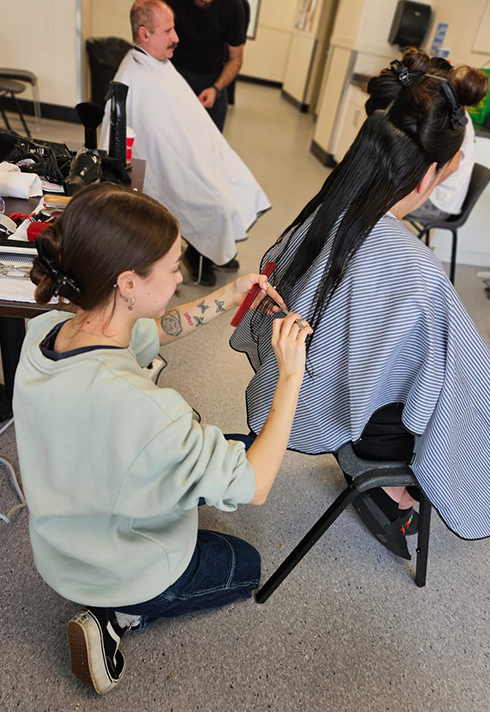 A lady benting down cutting her client's long dark hair
