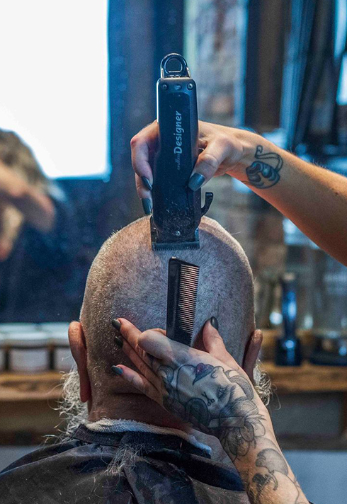 Alysha Osborne shaving off a gentleman's hair with a hair clipper. 